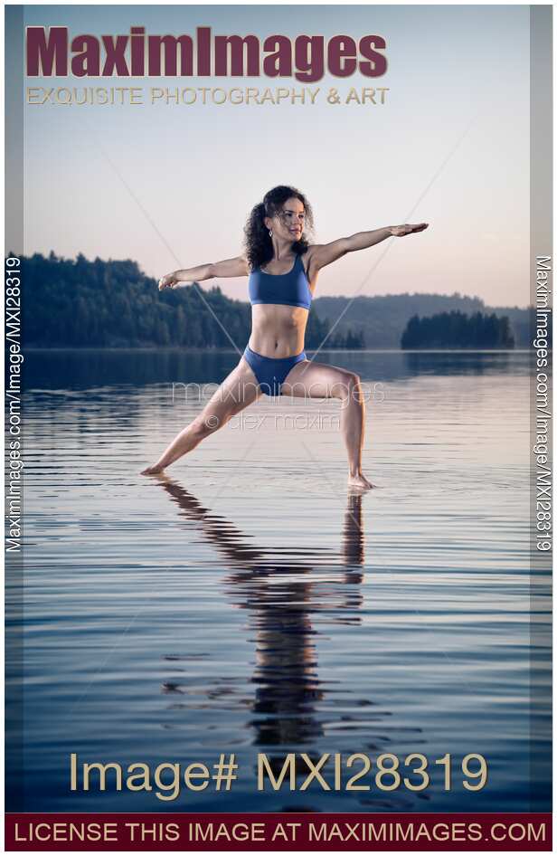 Young woman in blue swimsuit practicing yoga on the water Veerabhadrasana pose
