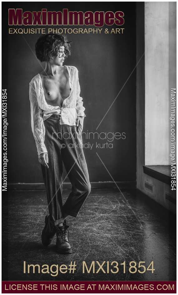Young woman in combat boots standing topless in empty room in unbuttoned shirt