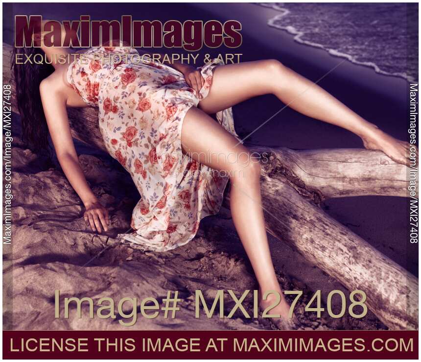 Young woman in dress lying on driftwood on a shore