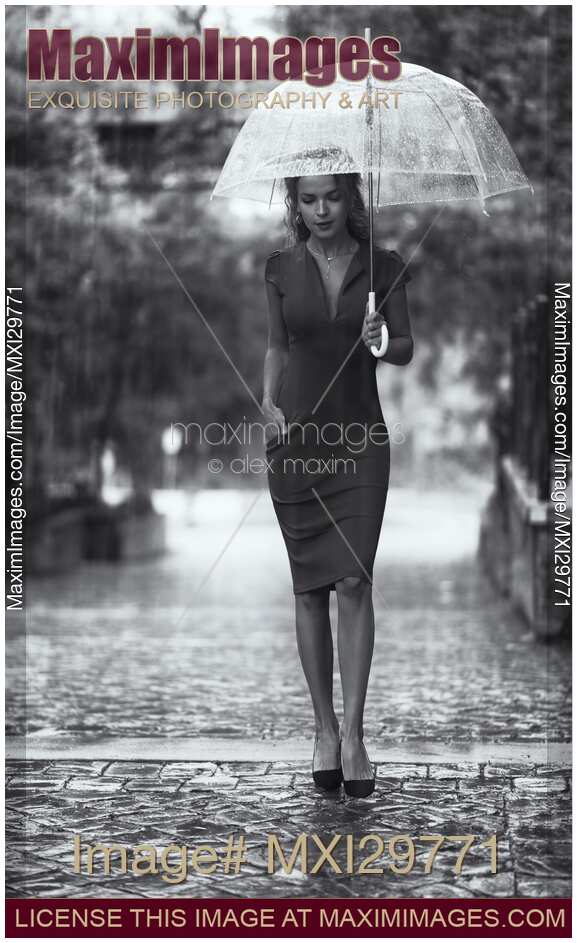 Young woman in elegant dress with umbrella walking thoughtfully in the rain Black and white