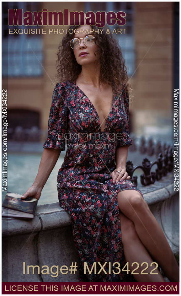 Young woman in elegant French dress sitting waiting by a street fountain with a book
