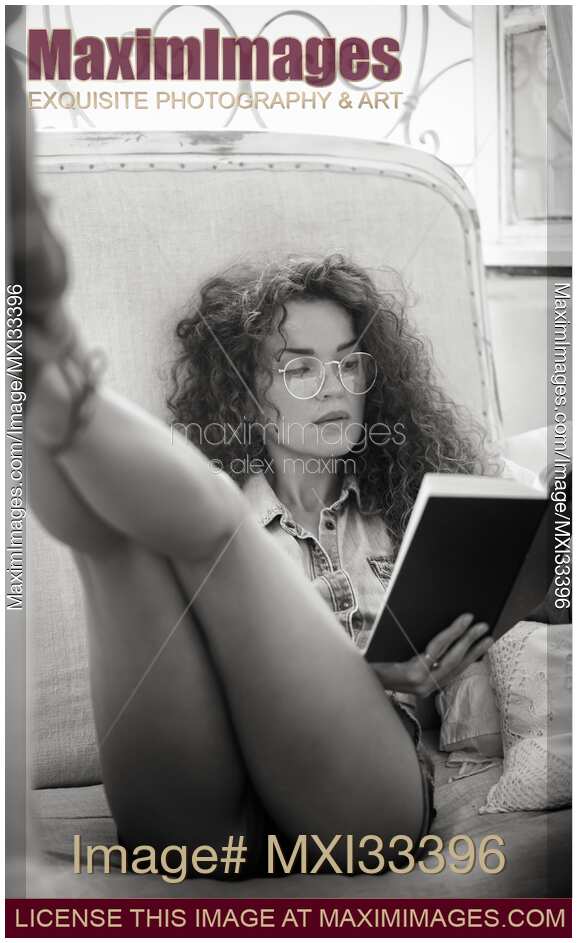 Young woman in glasses and tiny shorts with sexy long legs reading a book in a sensual pose Black and white portrait