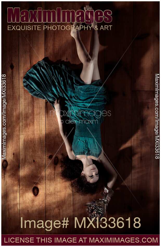 Young woman in green dress lying on the floor upside down with flowers