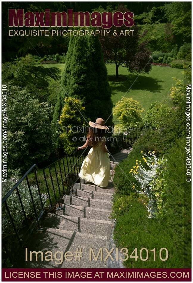 Young woman in summer dress and hat running down the stairs in a green garden