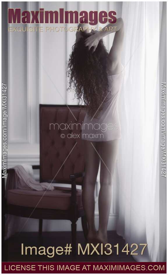 Young woman in underwear with bare legs standing on tiptoes stretching by the window in morning sunlight