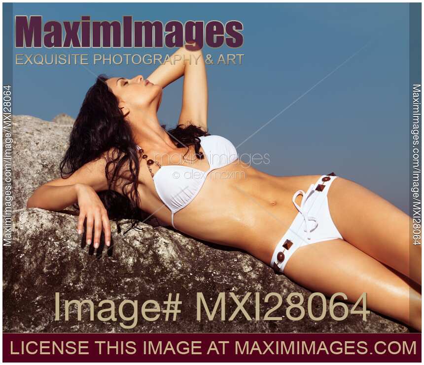 Young woman in white bikini sunbathing on rocks