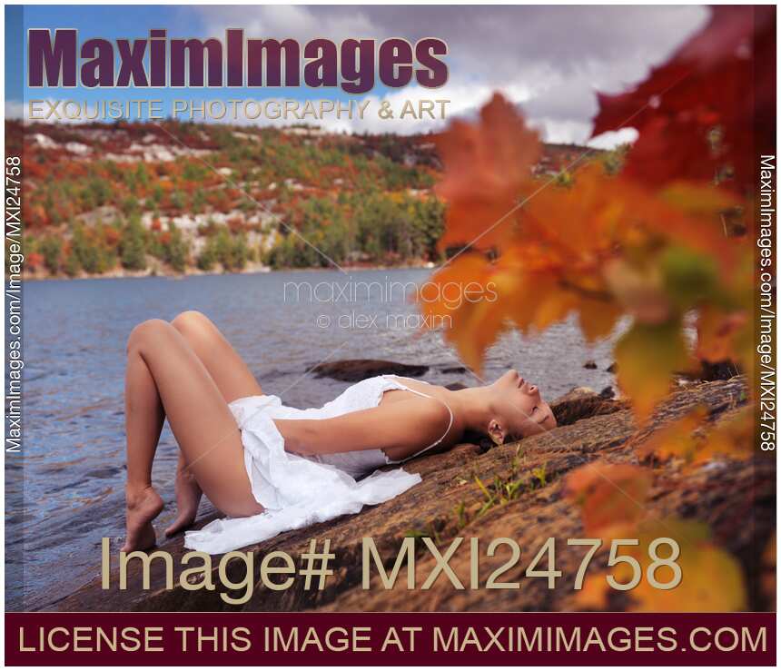 Young woman in white dress lying on shore of lake in fall