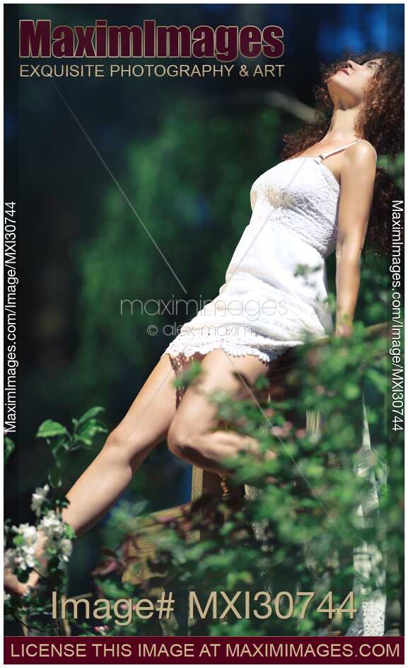 Young woman in white summer dress enjoying sunshine in a spring garden