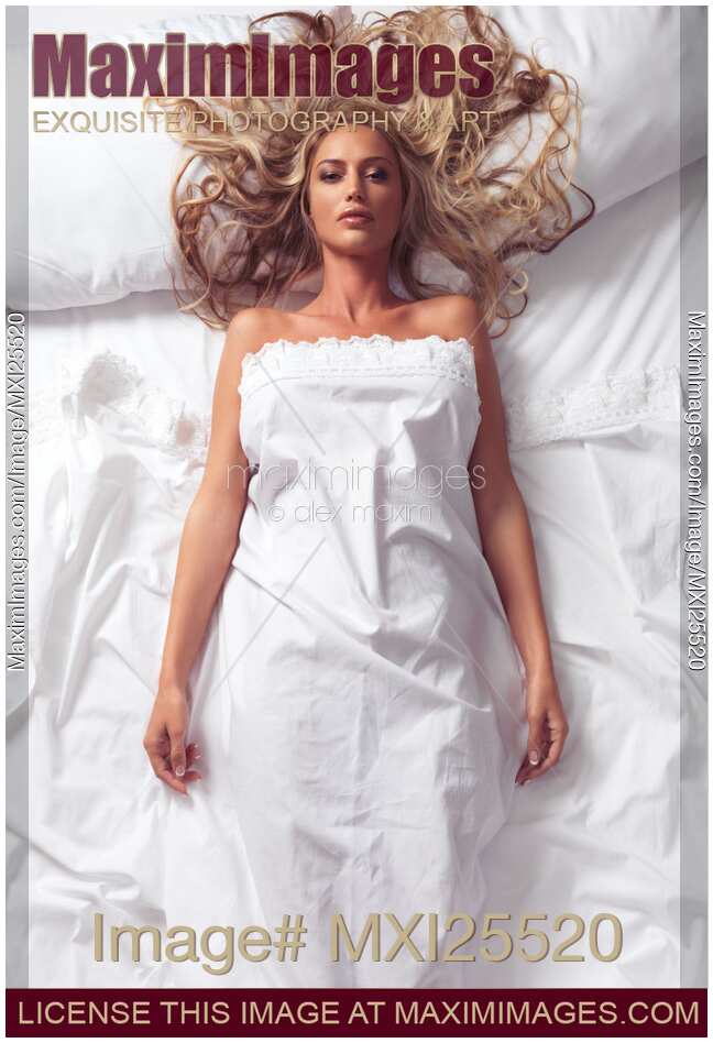 Young woman lying in bed under a sheet