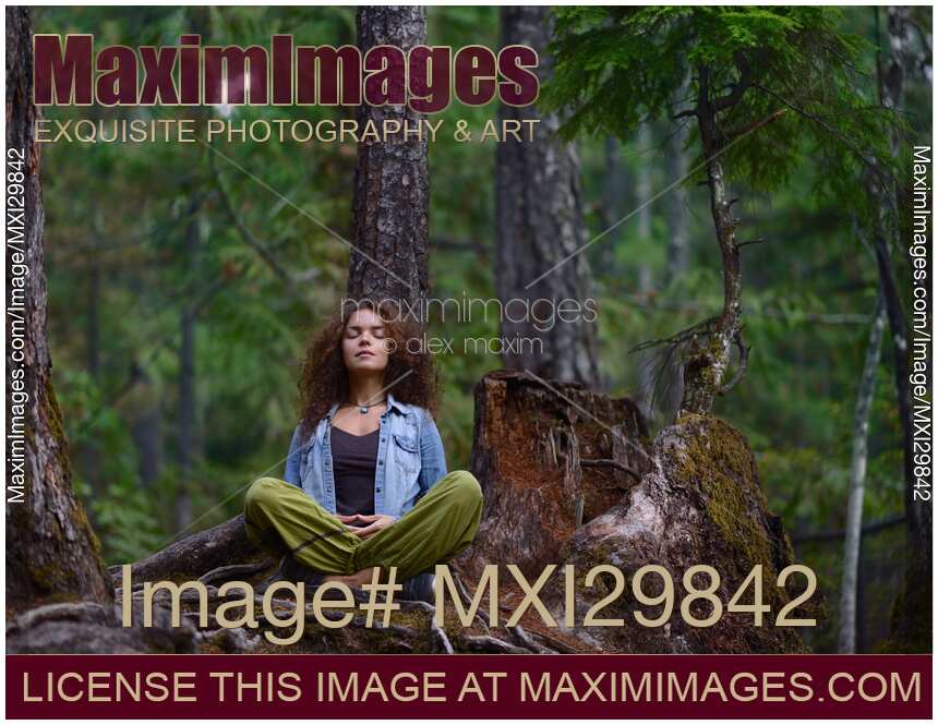 Young woman resting meditating in forest sitting against tree trunk in nature scenery