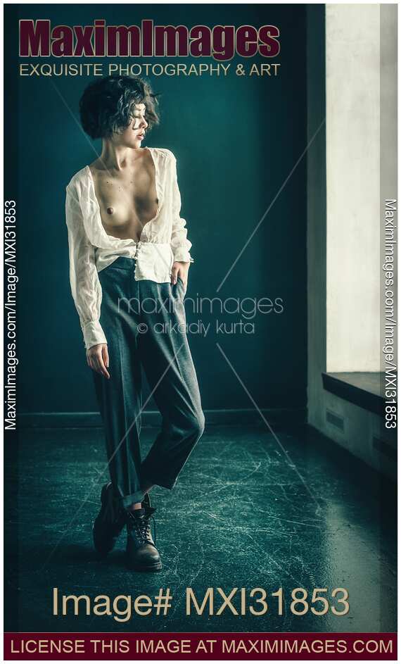 Young woman standing topless in an empty room with her shirt unbuttoned revealing her bare chest