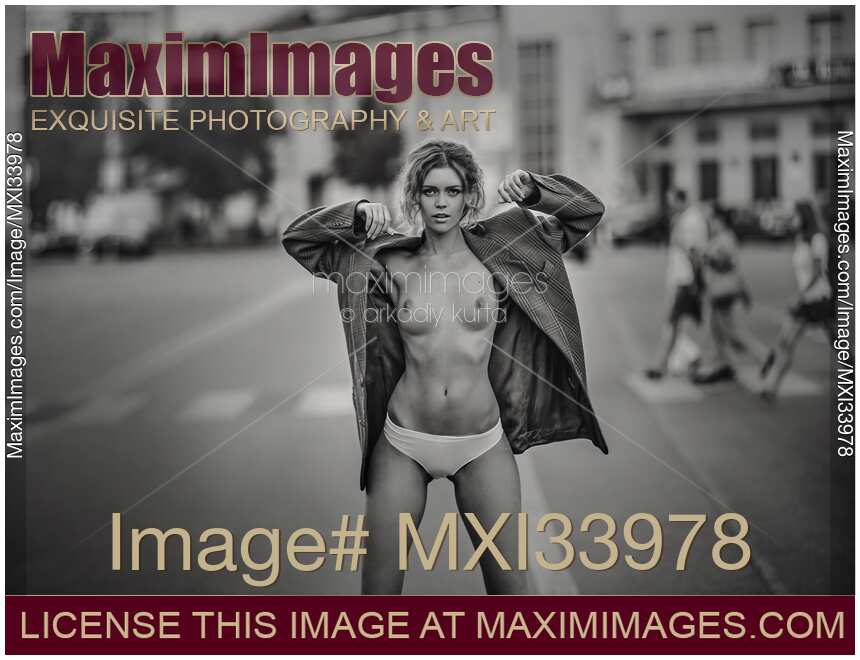 Young woman taking off her clothes standing half-naked on a city street. Black and white photo.