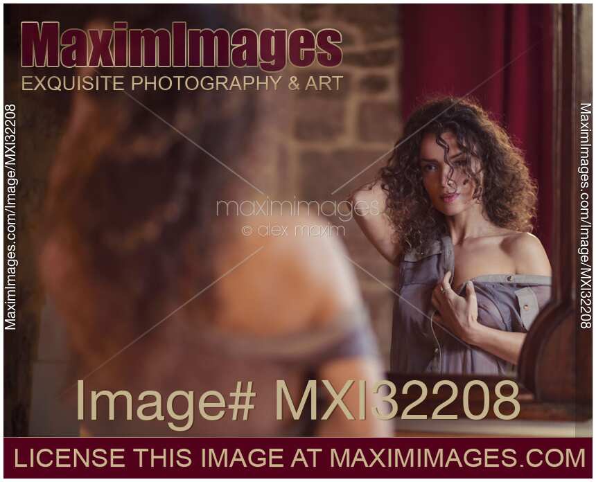 Young woman undressing in front of a mirror with a thoughtful look on her face