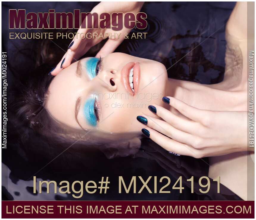 Young woman with blue makeup and manicure lying in water