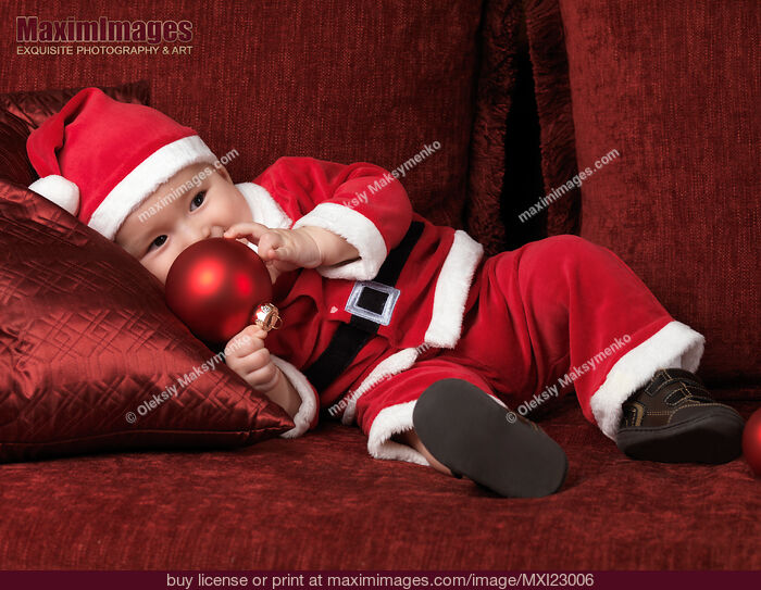 Stock photo of Baby Boy in Santas Costume with a Christmas Bauble Buy commercial use license at MaximImages