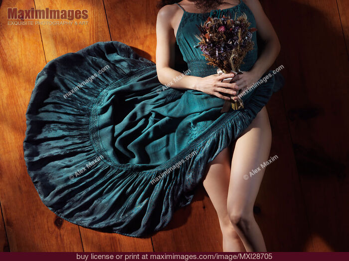 Stock photo of Sensual portrait of woman in blue dress with bare legs holding flowers lying on the floor Buy commercial use license at MaximImages