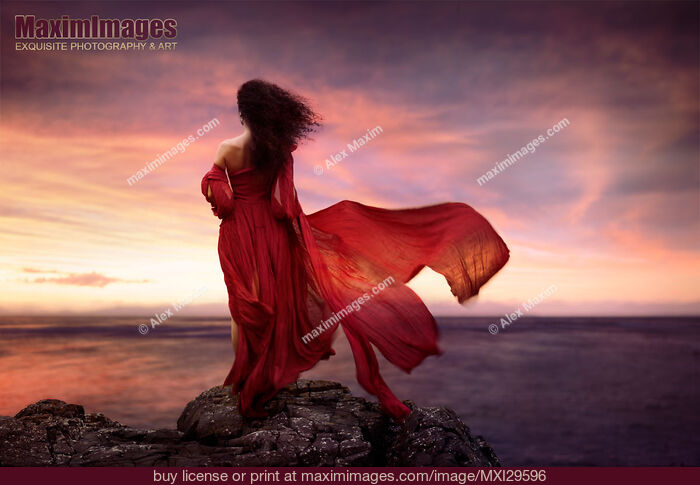 Stock photo of Woman in red dress flying in the wind looking at the ocean in sunset Buy commercial use license at MaximImages
