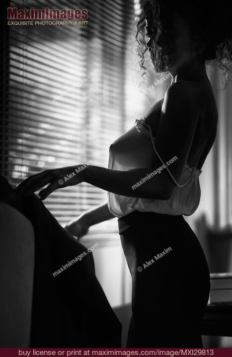 Stock photo of Sensual black and white boudoir portrait of woman in sexy sheer blouse standing by the window Buy commercial use license at MaximImages