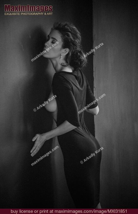 Stock photo of Sensual portrait of a woman in black dress revealing her bare breast leaning against a wall Buy commercial use license at MaximImages