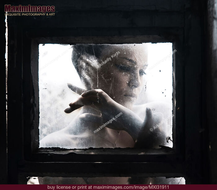 Stock photo of Dramatic expressive portrait of a woman face behind a closed dusty window glass Buy commercial use license at MaximImages
