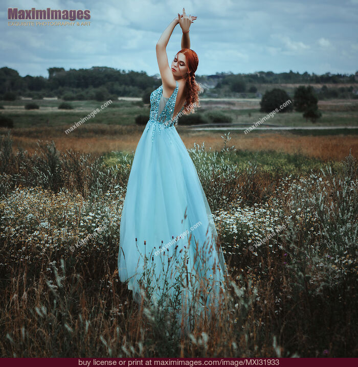 Stock photo of Red-haired woman in a long blue dress standing gracefully in a field of wild flowers Buy commercial use license at MaximImages