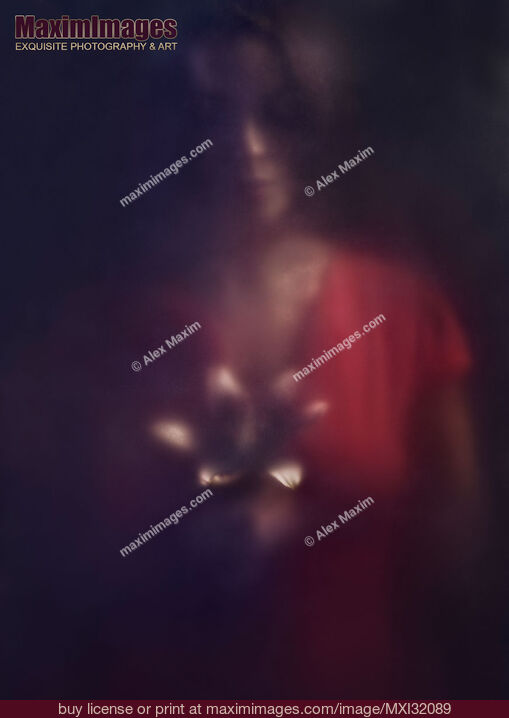 Stock photo of Mysterious dark portrait of a woman looking at a lily flower in her hands behind hazy glass in darkness Buy commercial use license at MaximImages