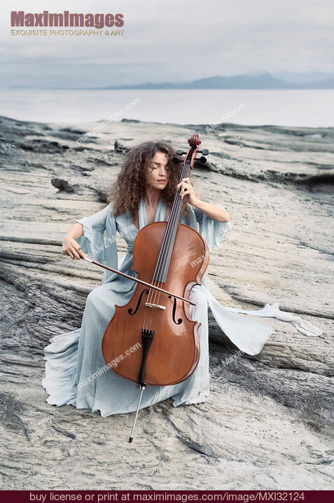 Stock photo of Woman thoughtfully playing cello on an ocean shore in sunrise scenery Buy commercial use license at MaximImages
