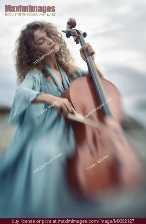 Stock photo of Beautiful young woman in a blue vintage dress passionately playing cello in sunrise nature scenery Buy commercial use license at MaximImages