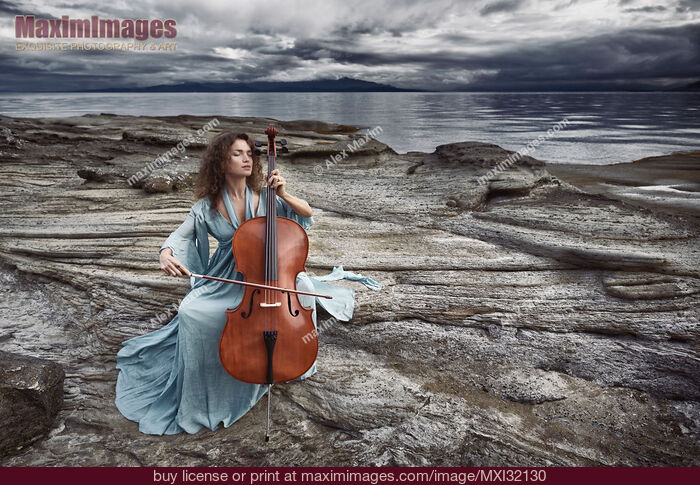 Stock photo of Woman with a tranquil thoughtful expression gracefully playing cello in dramatic stormy ocean shore scenery Buy commercial use license at MaximImages