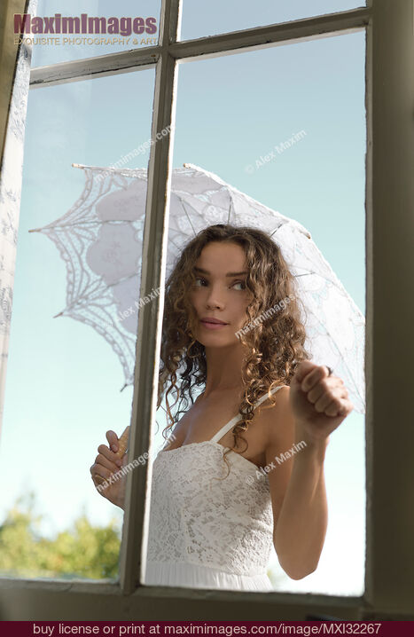 Stock photo of Young woman knocking on the door standing outside the house in summer dress with a French lace parasol Buy commercial use license at MaximImages