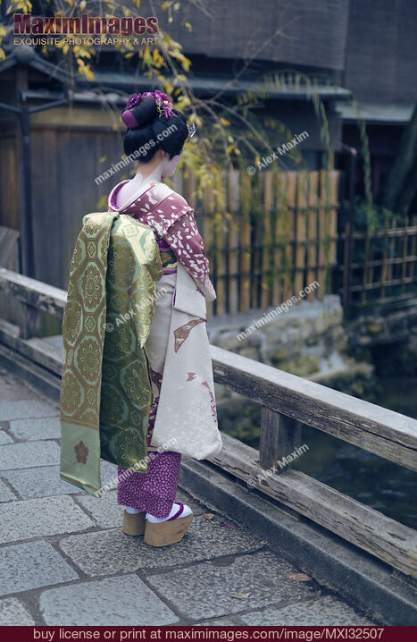Apprendista Maiko Geisha in kimono con lunga cintura obi e scarpe okobo da sola su un ponte a Kyoto Foto d'archivio di Apprendista Maiko Geisha in kimono con lunga cintura obi e scarpe okobo da sola su un ponte a Kyoto Acquista la licenza per uso commerciale su MaximImages