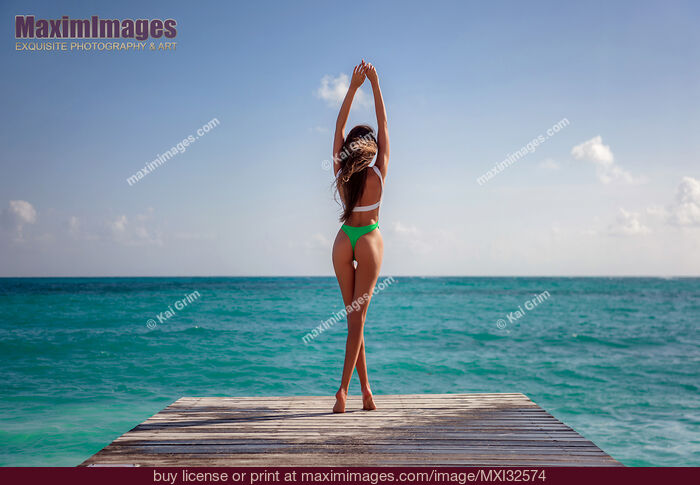 Stock photo of Sexy sun-tanned woman back in a fashion swimsuit standing on a pier overlooking blue ocean water Buy commercial use license at MaximImages