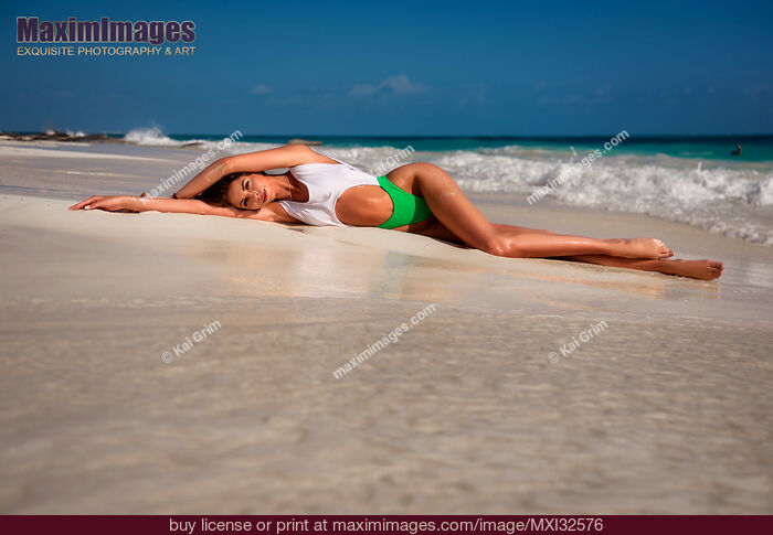 Stock photo of Sexy sun-tanned woman in a fashion bathing suit lying on white sandy shore of an ocean beach glamour portrait Buy commercial use license at MaximImages