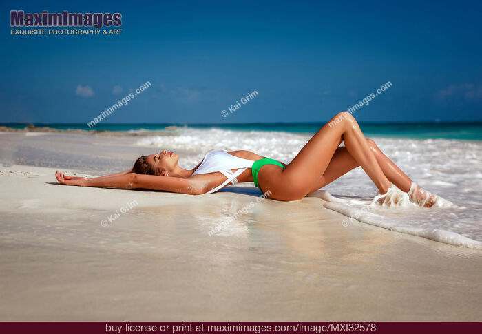 Stock photo of Beautiful sexy young woman in one-piece fashion swimsuit lying on sandy shore of ocean beach in Cancun Mexico Buy commercial use license at MaximImages
