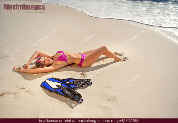 Stock photo of Sexy woman in pink bikini swimsuit lying on beach sand with goggles and swimming fins Caribbean Sea Buy commercial use license at MaximImages
