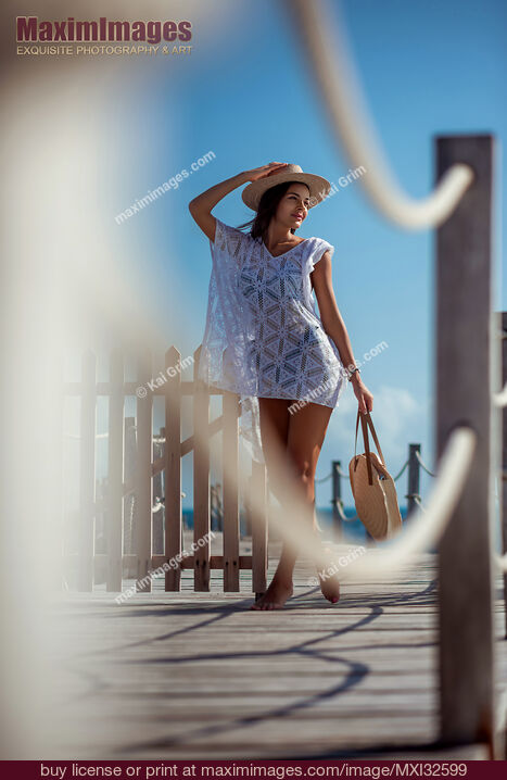 Stock photo of Woman in beach dress and hat with tote bag walking along a sea front boardwalk in summer Cancun Buy commercial use license at MaximImages