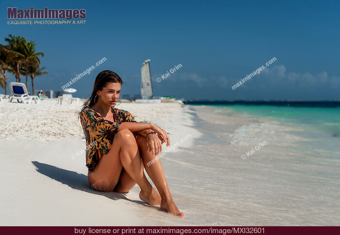 Stock photo of Beautiful woman in beachwear sitting on a white sandy shore of Caribbean Sea beach in Cancun, Mexico Buy commercial use license at MaximImages
