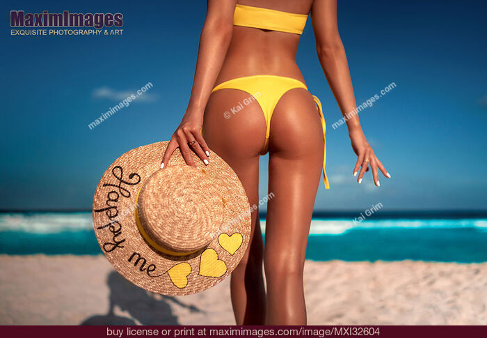 Stock photo of Sexy sun-tanned woman in a bright swimsuit with a straw sun hat at a tropical beach closeup of her back and buttock Buy commercial use license at MaximImages