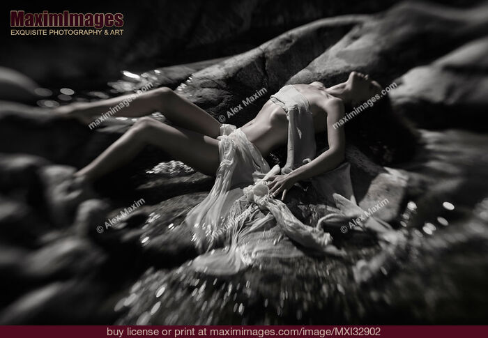 Stock photo of Beautiful nude woman lying on river rocks her naked barely covered body blending with rocky landscape Black and white Buy commercial use license at MaximImages