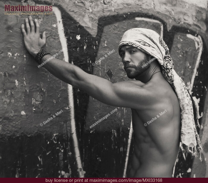 Stock photo of Portrait of a sexy handsome bearded man with bare torso wearing bandana leaning against graffiti wall Black and white Buy commercial use license at MaximImages