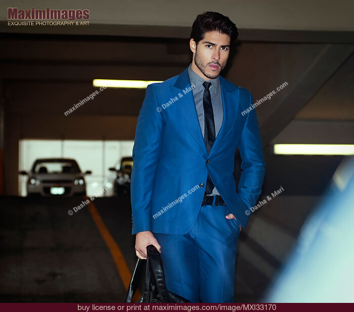 Stock photo of Handsome man in a classic elegant blue business suit walking to his car in indoor parking lot Buy commercial use license at MaximImages