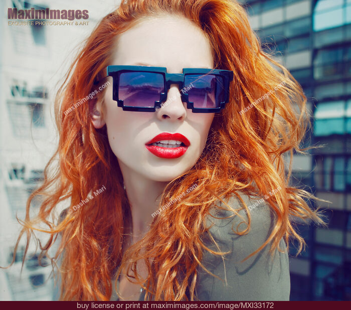 Stock photo of Retro fashion portrait of a young red-haired lady in funky avant-garde sunglasses on a city rooftop Buy commercial use license at MaximImages