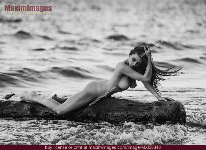 Stock photo of Woman posing nude on driftwood in stormy sea water Fine art nude photography Buy commercial use license at MaximImages