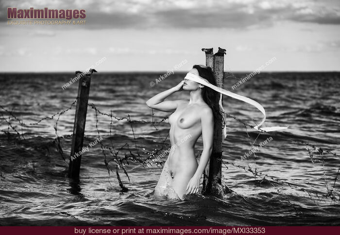 Stock photo of Woman standing naked in water against a rusty post with a blindfold Fine art nude black and white Buy commercial use license at MaximImages