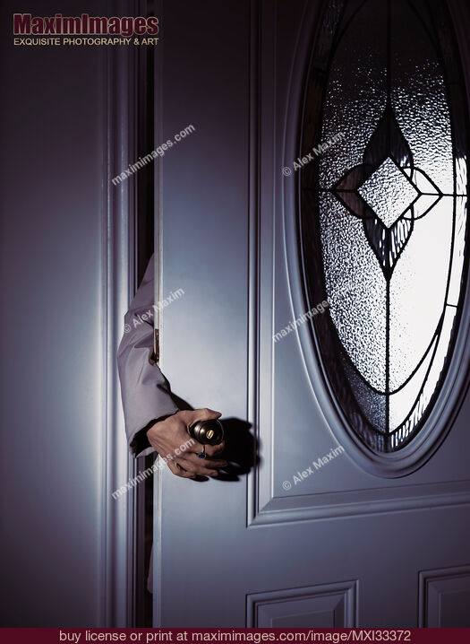 Stock photo of Woman's hand reaching for a door handle from behind a dark shadowy house front door Buy commercial use license at MaximImages