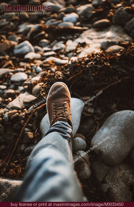 Stock photo of Closeup of a man's leg in brown hiking shoes walking on a pebble beach Buy commercial use license at MaximImages