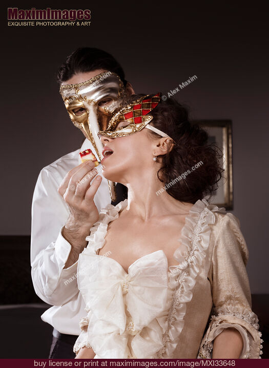 Stock photo of Sensual couple portrait of masked Casanova man seducing beautiful lady in vintage Venetian dress and carnival mask with cake pastry Buy commercial use license at MaximImages