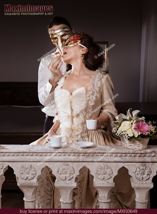Stock photo of Sensual couple portrait of masked man tempting beautiful lady in vintage Venetian carnival dress and mask with pastry. Casanova. Buy commercial use license at MaximImages