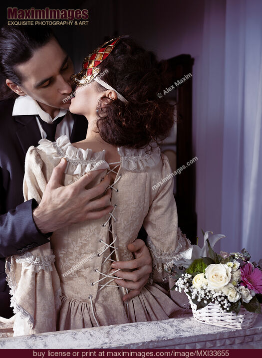 Stock photo of Sensual romantic portrait of a kissing couple. Elegant man unlacing corset dress back of a woman in Venetian carnival mask. Buy commercial use license at MaximImages
