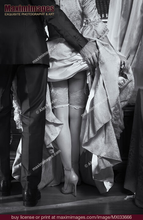 Stock photo of Man raising up woman's dress skirt revealing her sexy legs in stockings and high heels. Black and white rear view. Buy commercial use license at MaximImages